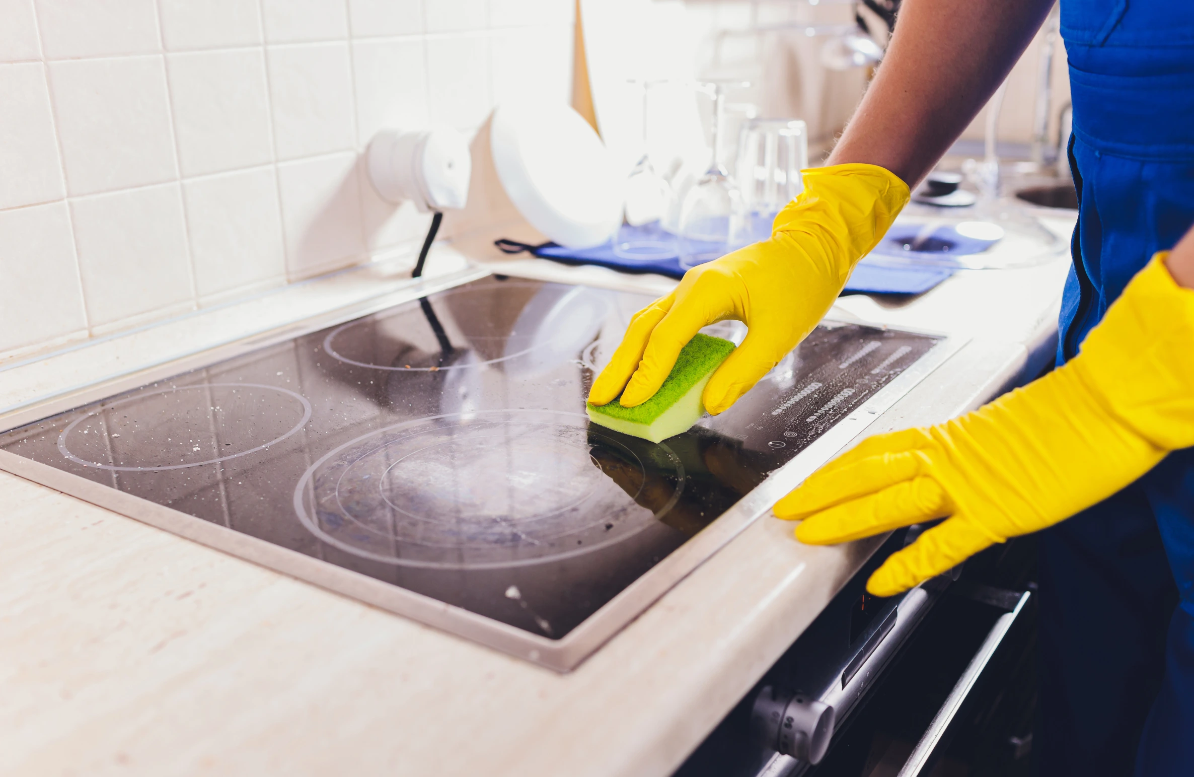 A person wearing yellow gloves cleaning a kitchen stove with an eco-friendly sponge, representing Why Biodegradable Cleaners Are the Future of Sustainable Living.